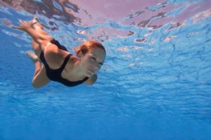 Attractive female swimming under the water surface with eyes opened. Focused on face, polarizing filter, convenient copy space